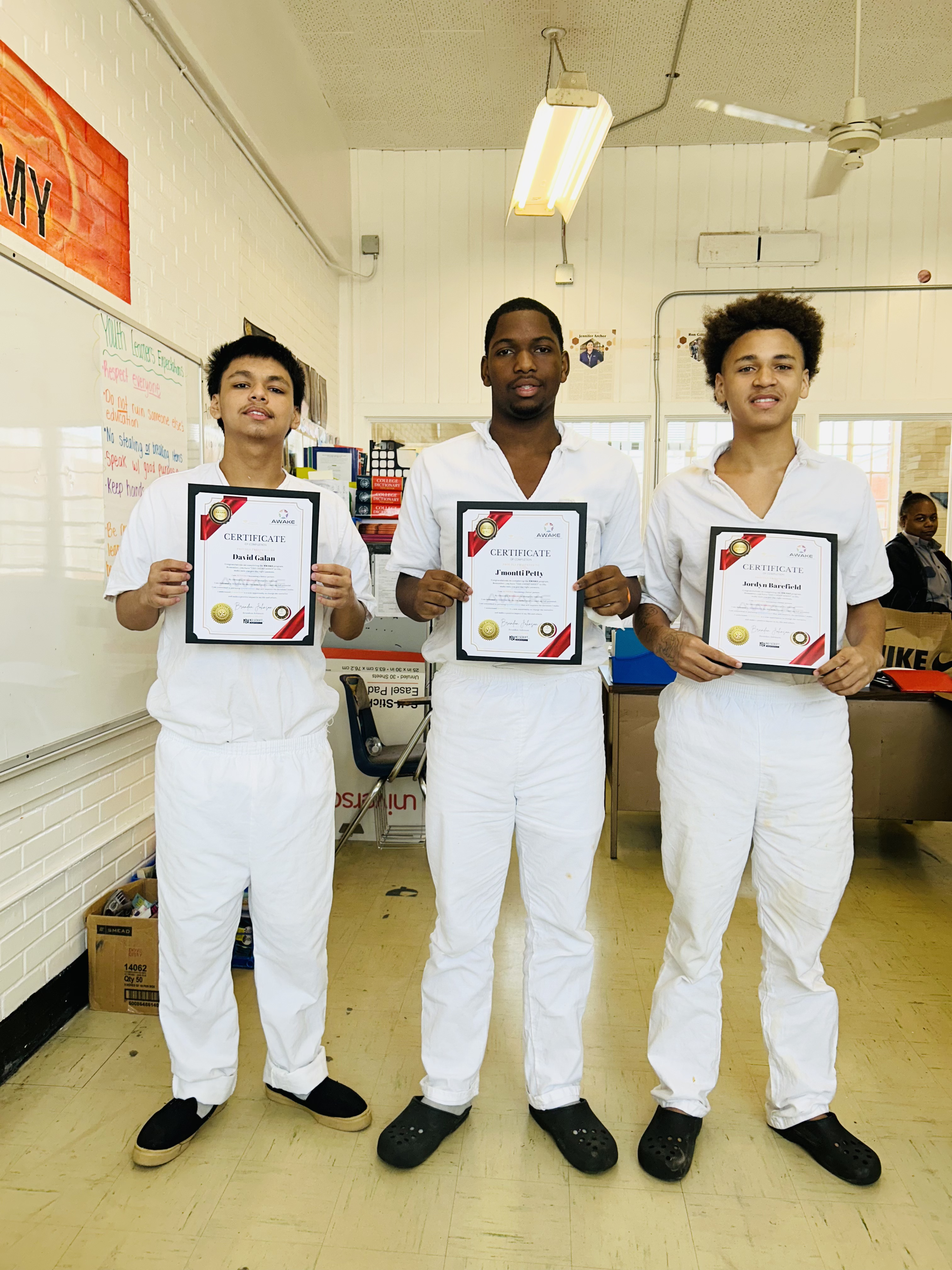 Three young men in a classroom holding their AWAKE Program certificates of completion