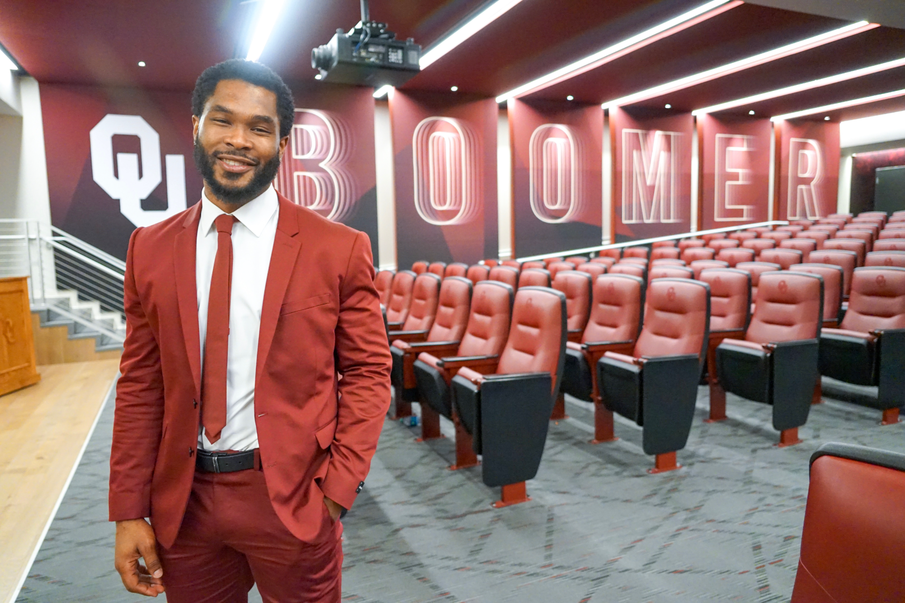 Brandon Johnson in a crimson suit standing in an auditorium at the University of Oklahoma